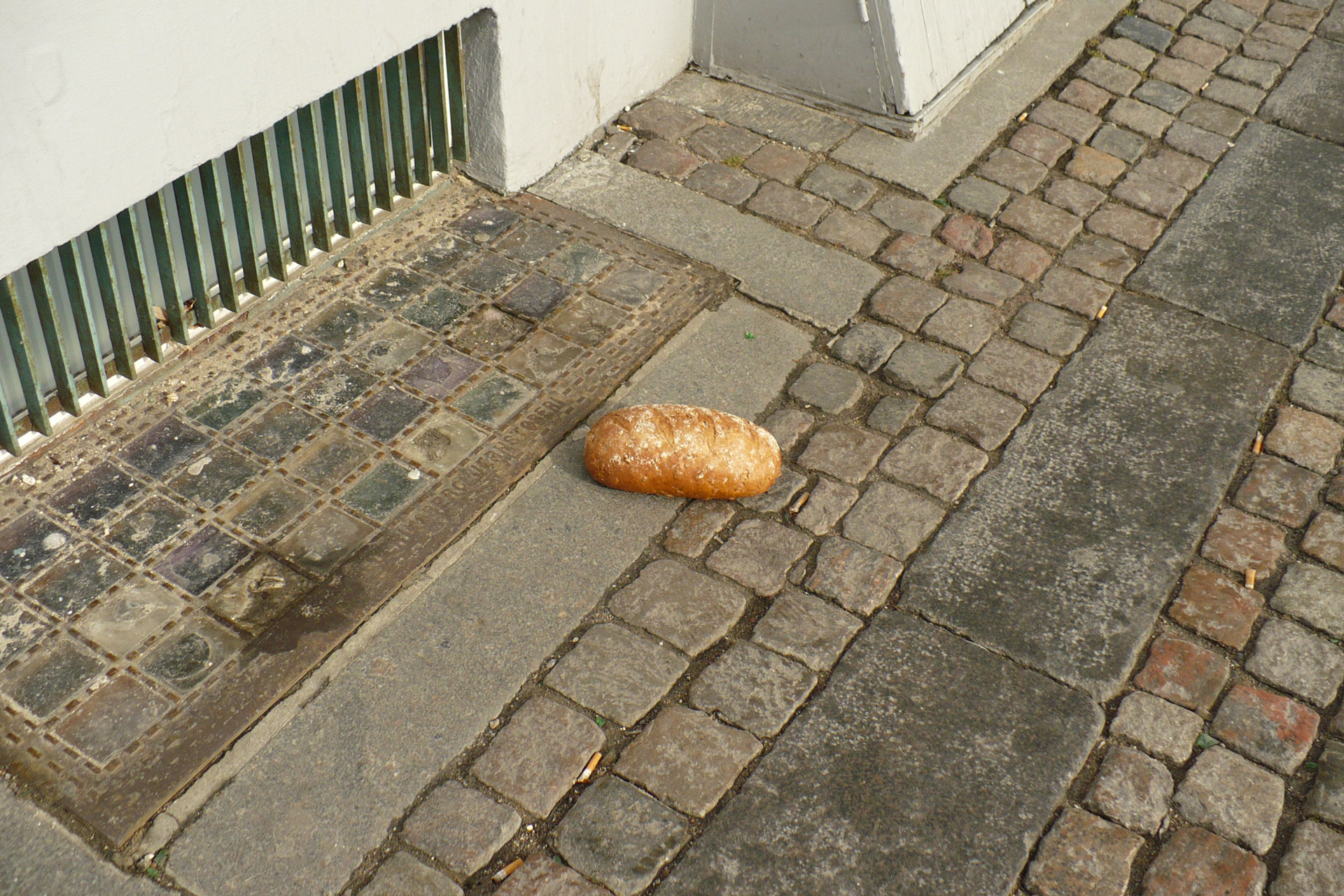 A loaf of bread on the sidewalk next to a basement window grill